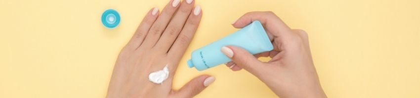 A woman putting on sunscreen to prevent freckles in her hands.