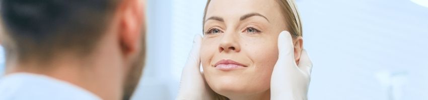 Cosmetic surgeon examines beautiful woman's face.