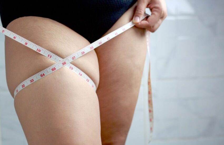 A woman is measuring her thigh, which has saddlebags.