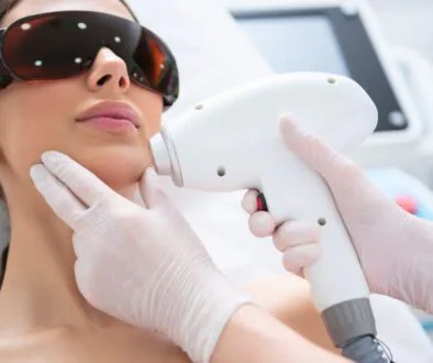 Patient undergoing BBL halo laser treatment with protective eyewear while a specialist uses a laser device on her face.