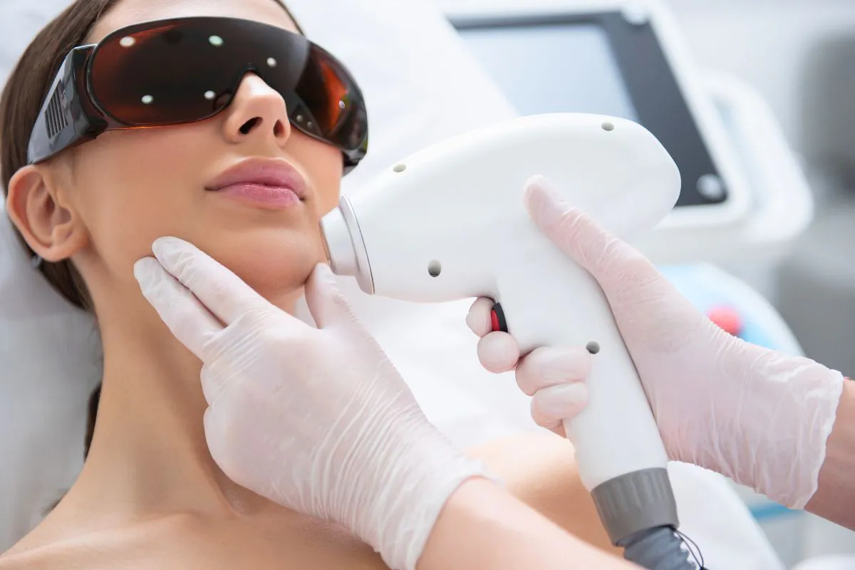 Patient undergoing BBL halo laser treatment with protective eyewear while a specialist uses a laser device on her face.